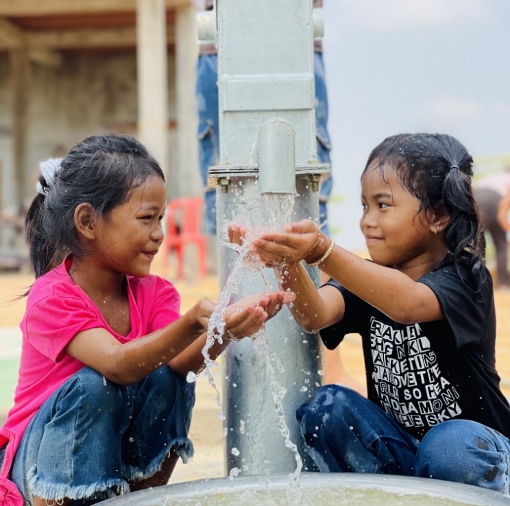 Children sitting beside a well while water if pouring out