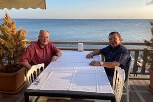 Eric Vess sitting at a table with P.R. Misra wth the ocean behind them
