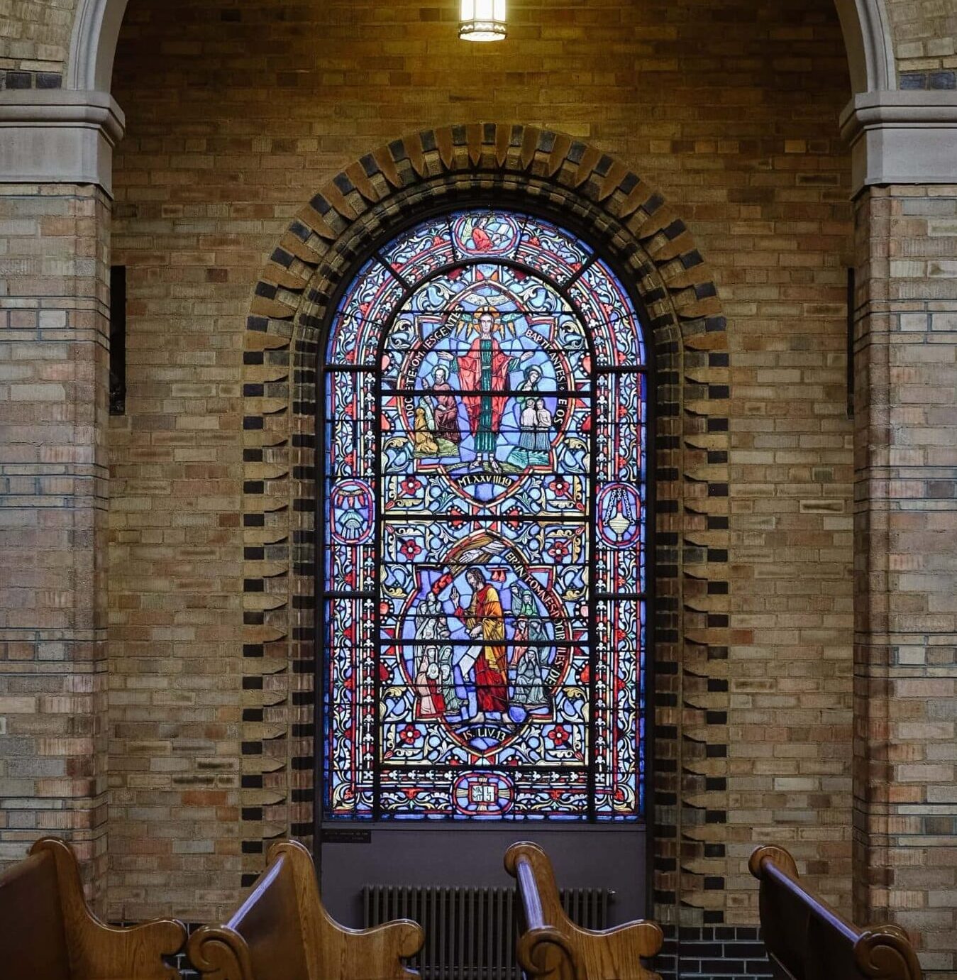 An arched stained glass window in the inside of a church with church pews in front of it