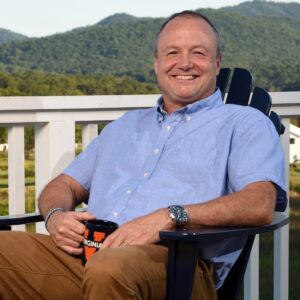 Oliver Asher sitting in a chair on a porch outside with mountains in the background