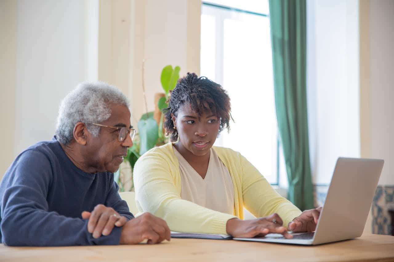 Young woman helping an elderly man with a task using a laptop in a home environtment